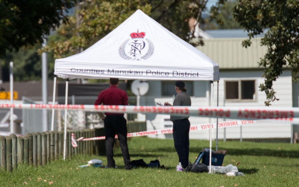 Police gather evidence opposite the train station in Papakura after a shooting early this morning that left one man dead and another seriously injured.