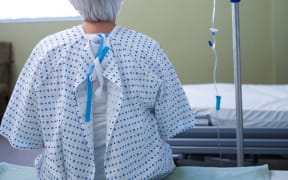 Rear-view of senior patient sitting on bed in hospital