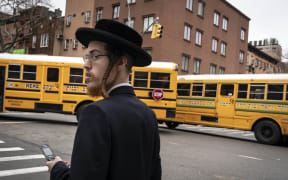 A man walks past school buses in a South Williamsburg neighborhood. A public health emergency has been declared in the  area.