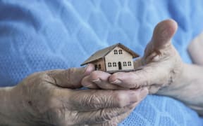 closeup wrinkled hands holding a small wooden house