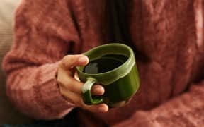 A person in a brown sweater holds a green cup of water.