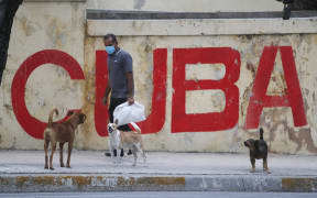 A man and dogs walk in front of a graffiti with the word "Cuba" in Havana, Cuba, on January 11, 2021.