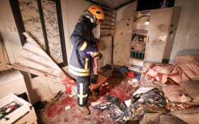 A Palestinian civil defence worker inspects the site where shrapnel from projectiles fell in Beit Awa near the Israeli-occupied West Bank city of Hebron on March 18, 2026. Four Palestinian women were killed in the occupied West Bank on March 18 by falling shrapnel, emergency responders said, shortly after Israel's military reported another Iranian missile barrage. The Palestinian Red Crescent confirmed four fatalities, all women, and six injuries ranging from moderate to minor, in the Beit Awa area near Hebron, marking the first Palestinian deaths in the ongoing Middle East war. (Photo by HAZEM BADER / AFP)