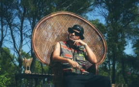 A relaxed man sits in a wicker chair outside.
