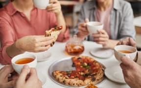 Close-up of woman holding piece of pizza and having lunch together with her family at the table
