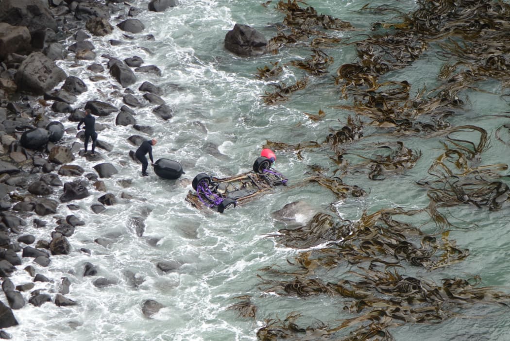 Police attach black floats to the car wreck in preparation for its removal from the bay.