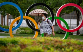 A woman holds an umbrella walking past the Olympic Rings in front of Japan Olympic Museum in Tokyo on July 8, 2021. (Photo by Philip FONG / AFP)