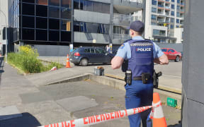 A police officer on Nelson St, Auckland, after a man suffered a minor gunshot injury and a vehicle was found with bullet holes.