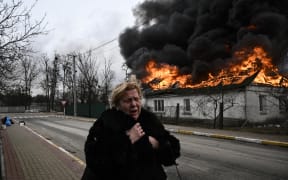 A woman stands in front of house burning after being shelled in Irpin, outside Kyiv, on 4 March 4, 2022. More than 1.2 million people fled Ukraine into neighbouring countries since Russia launched its full-scale invasion on 24 February, UN figures on 4 March showed.