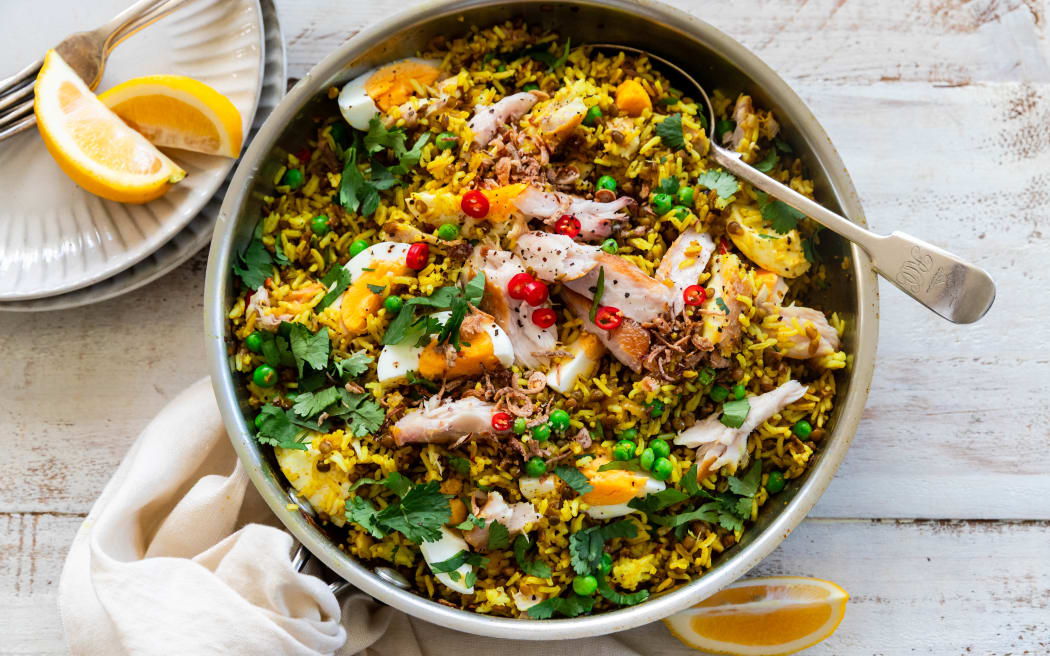 A bowl of kedgeree with lentils, peas, chilli, smoked fish and herbs, garnished with lemon.