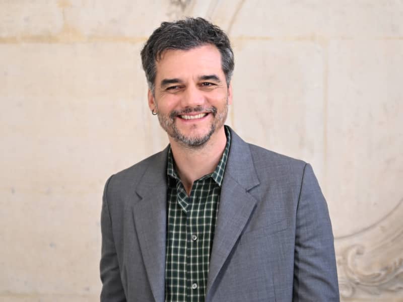 Wagner Moura is a smiling bearded man in a grey suit jacket.