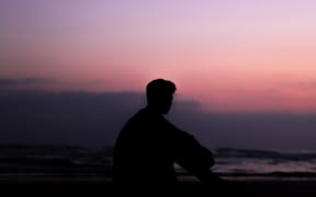 A young person with short hair looks into the sunset.
