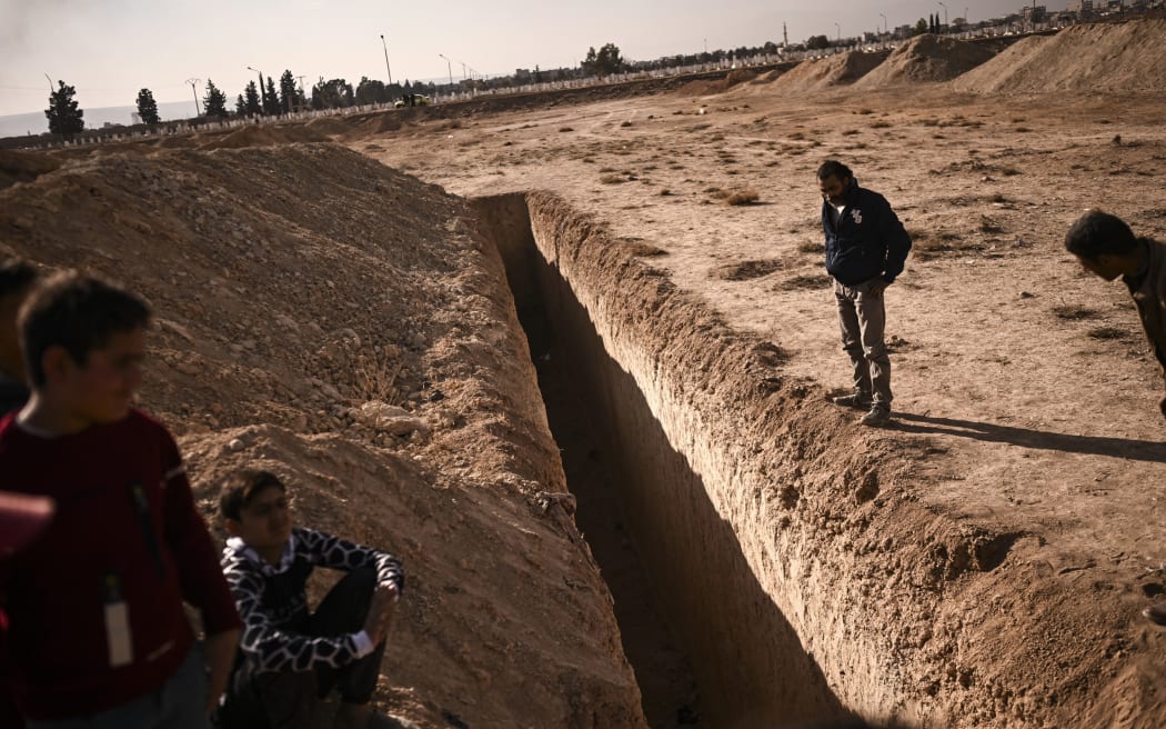 People stand next to a trench believed to be used as a mass grave on the outskirts of Damascus on 16 December.