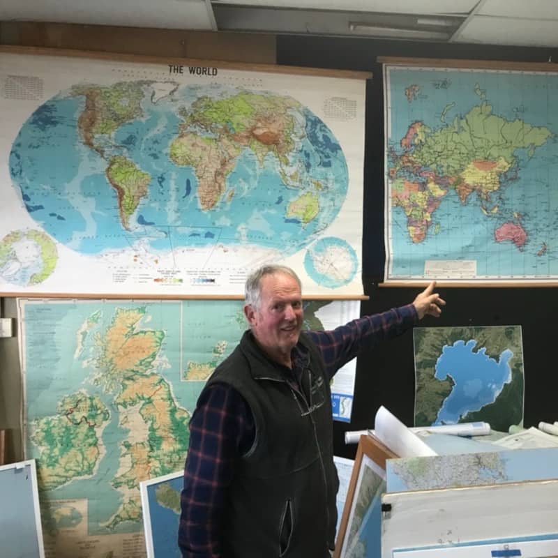 Murray Jones pointing at a world map on the wall of his shop.