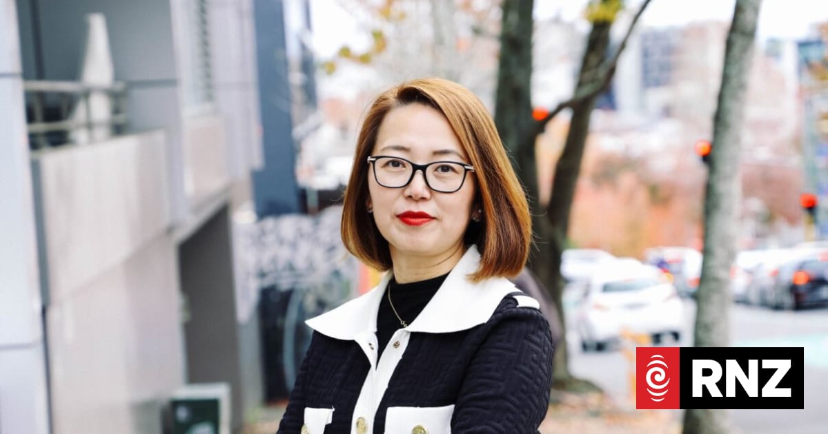 A woman in a dark jacket and glasses standing on a city street.