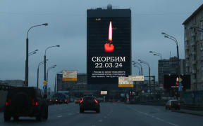 Cars drive past an advertising screen on the facade of a building displaying an image of a lit candle and the slogan "(We) Mourn 22.03.24" in Moscow on March 23, 2024, a day after a gun attack on the Crocus City Hall in Russia's Krasnogorsk. Camouflaged assailants opened fire at the packed Crocus City Hall in Moscow's northern suburb of Krasnogorsk on March 22, 2024, evening ahead of a concert by Soviet-era rock band Piknik in the deadliest attack in Russia for at least a decade. Russia on March 23, 2024, said it had arrested 11 people - including four gunmen - over the attack on a Moscow concert hall claimed by Islamic State, as the death toll rose to 133 people. (Photo by STRINGER / AFP)
