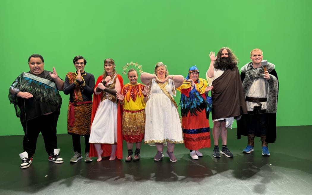 A group of performers pose in costume in front of a green screen.