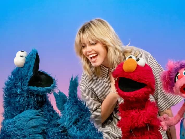A blonde woman laughs with three puppets.