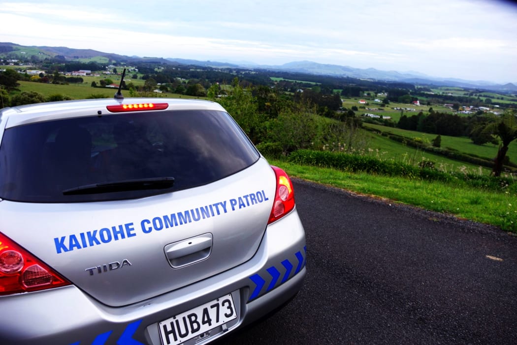 A silver community watch patrol car, perch on a hill about a farm. Locals patrol the region doing work they say the police should be doing
