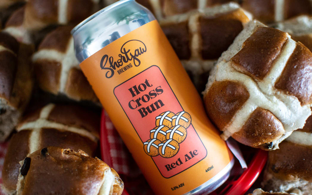 A can of Shortjaw Brewing Hot Cross Bun Red Ale lying amongst some hot cross buns