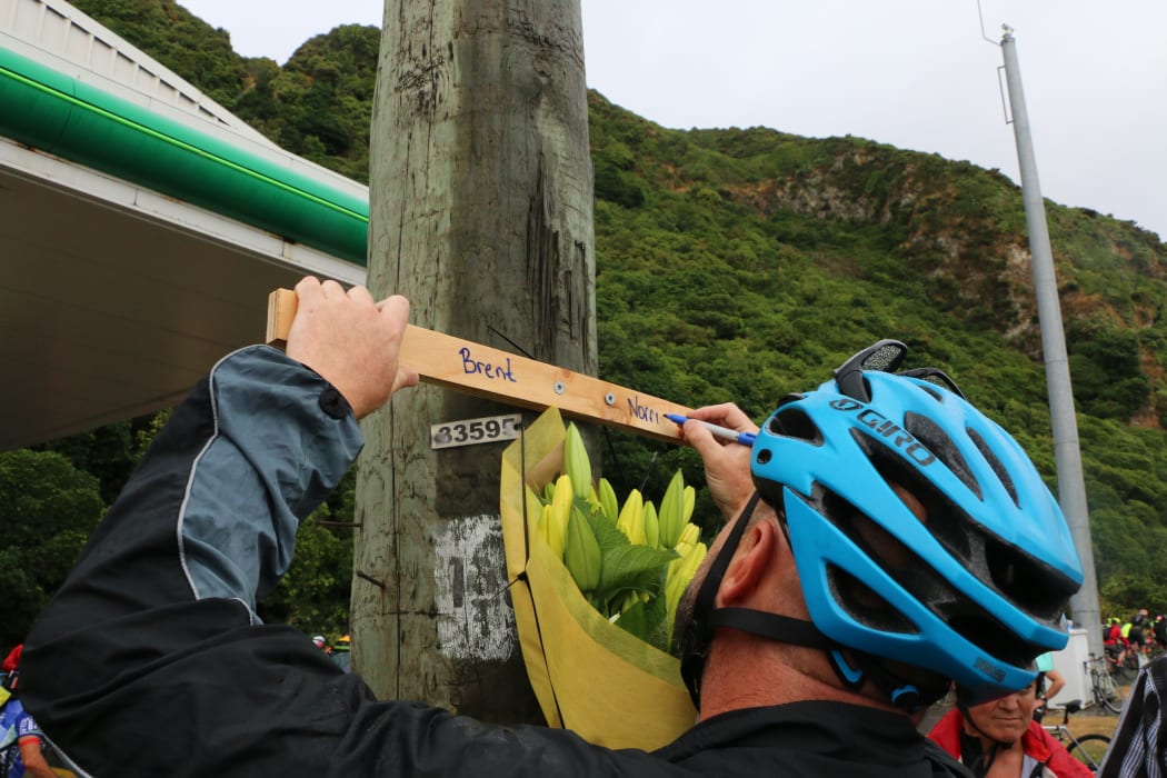 A cyclist writes on the tribute cross on the side of the Hutt Road.