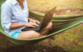 Women travel in natural sitting in the hammock and working in a natural park using a notebook.