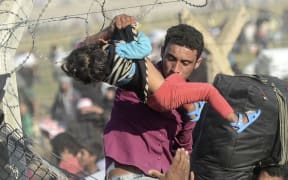 A man carries a girl as Syrians fleeing the war pass through broken down border fences to enter Turkish territory.