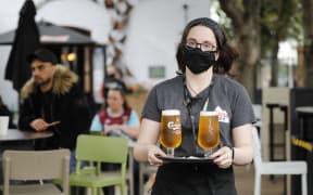 A member of bar staff wearing PPE (personal protective equipment) in the form of a face mask, serves customers with drinks outside the Wetherspoon pub, Goldengrove in Stratford in east London on July 4, 2020, as restrictions are further eased during the novel coronavirus COVID-19 pandemic.