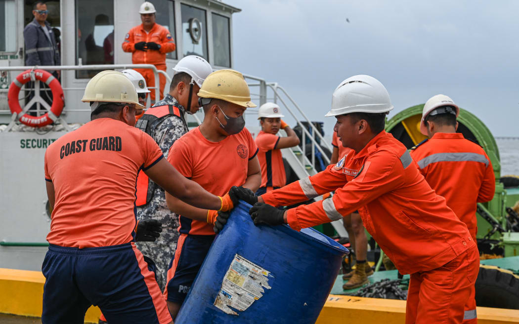 Coast guard personnel and crew of a private company load a barrel of oil spill dispersant to be used in the oil spill response, at a port in Limay, Bataan on July 26, 2024. A Philippine-flagged tanker carrying 1.4 million litres of industrial fuel oil capsized and sank off Manila on July 25, authorities said, as they raced against time to contain the spill. (Photo by Jam Sta Rosa / AFP)