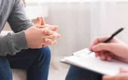 Therapist writing notes during counseling session with single man sitting on couch, panorama, empty space