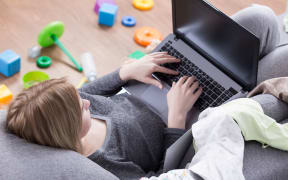 Young and tired woman lying on sofa with laptop, toys lying on the floor