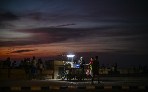 A street vendor uses a portable lamp to sell goods along the Malecon during a nationwide blackout in Havana on July 6, 2026. Cuba on July 6 suffered its third nationwide power outage since the start of the year, the state electricity company said. The impoverished island was already struggling to keep the lights on before US President Donald Trump in January imposed an oil blockade, which has depleted the already dwindling supply of fuel for Cuba’s power plants. (Photo by ADALBERTO ROQUE / AFP)