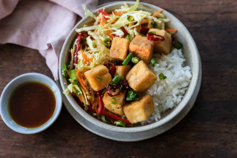 A round bowl of salt and pepper tofu cubes, served with slaw and rice.