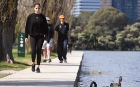 A woman passes a swan while exercising in Melbourne on September 16, 2021, as the state government announced a loosening of Covid-19 restrictions.