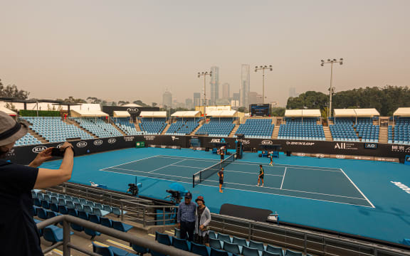 Tourists pose for a photo in the stands of one of the outside courts at Melbourne Park as the horizon is covered with thick smoke haze in Melbourne on January 15, 2020, ahead of the Australian Open tennis tournament.