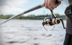 Hand holding a fishing rod with reel.