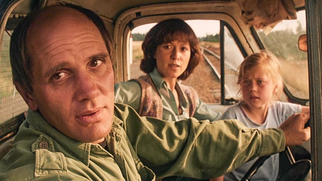 A movie still from Roger Donaldson's film Smash Palace featuring Bruno Lawrence, Anna Jemison and Greer Robson in a truck parked on some train tracks.