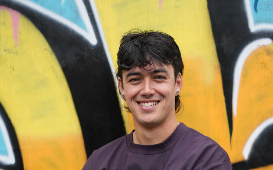 A image of ICYMI presenter Tāne Rolfe in front of a wall of street art.
