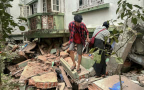 Residents walk over debris next to a damaged building in Naypyidaw on March 28, 2025, after an earthquake in central Myanmar. A powerful earthquake rocked central Myanmar on March 28, buckling roads in capital Naypyidaw, damaging buildings and forcing people to flee into the streets in neighbouring Thailand. (Photo by Sai Aung MAIN / AFP)
