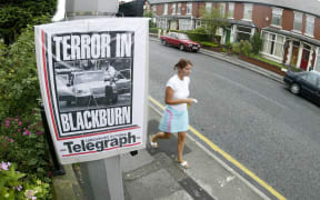 A pedestrian walks past a newspaper front page announcing the arrest of suspects on terrorism charges on Old Preston Road in Blackburn, Lancashire.