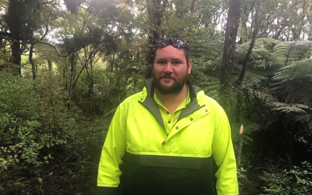 A man wearing hi-vis looking directly at the camera. He is in the bush on Aotea Great Barrier Island