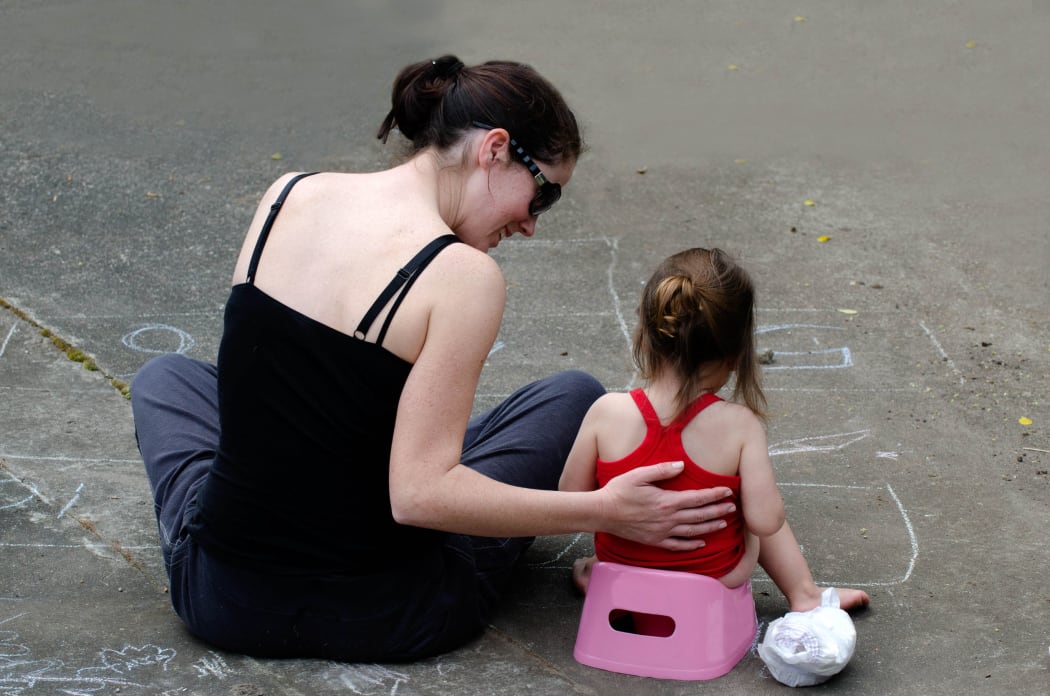 A photo of a young mother training her daughter to use the potty outdoor.