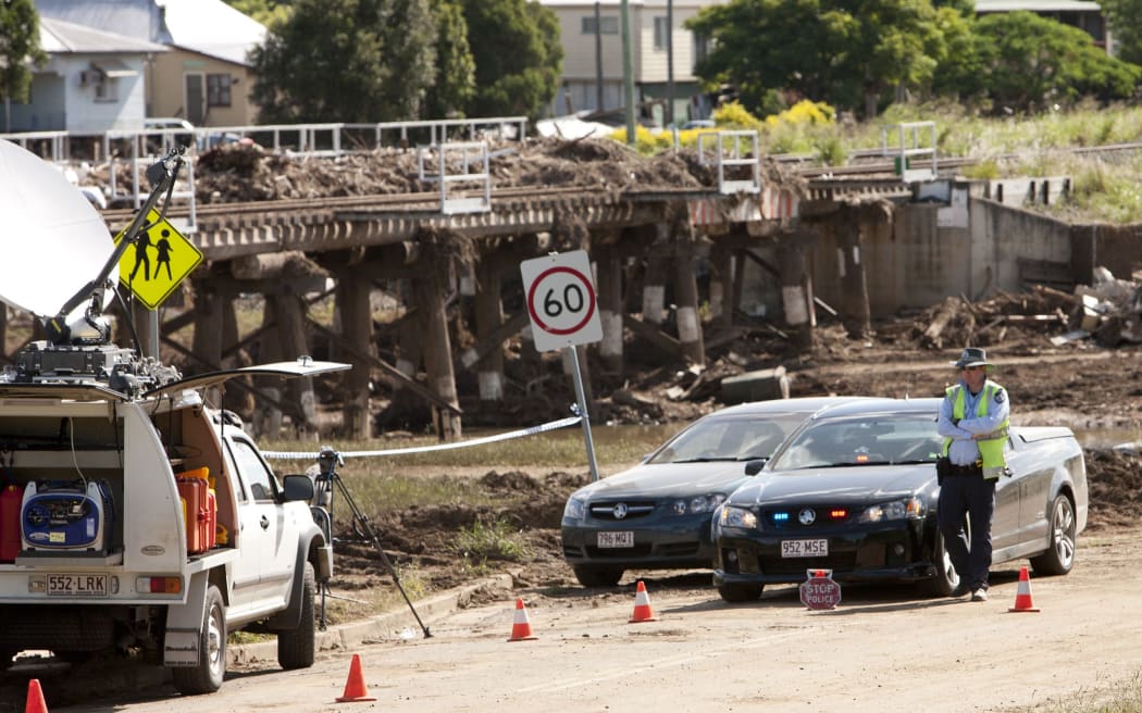 A policeman sits at a roadblock where heavy damage was caused by recent flooding in the town of Grantham on January 16, 2011. Queensland has had a six-week flood crisis, where floodwaters swallowed an area the size of France and Germany combined, culminating in the swamping last week of Brisbane, Australia's third largest city, and utter devastation of towns to the west, like Grantham.      AFP PHOTO / Eddie Safarik (Photo by EDDIE SAFARIK / AFP)