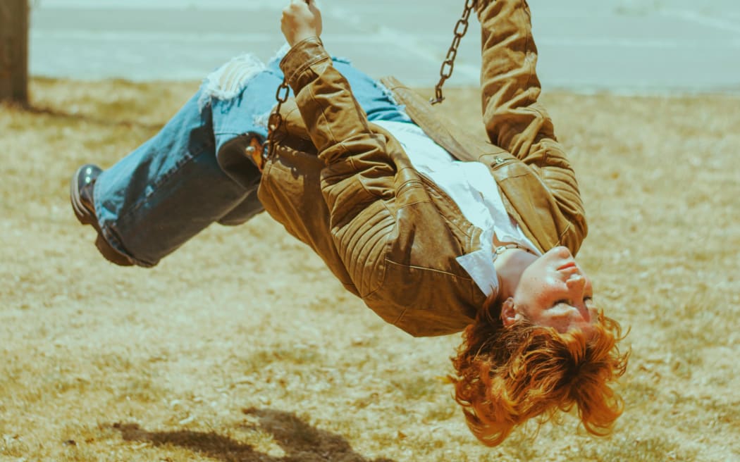A redhead teenager hanging upside down on a swing