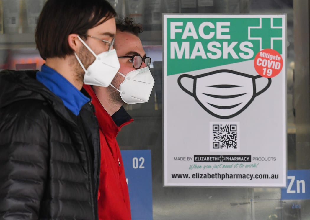 People wearing face masks walk past a sign advertising masks in Melbourne on July 20, 2020.