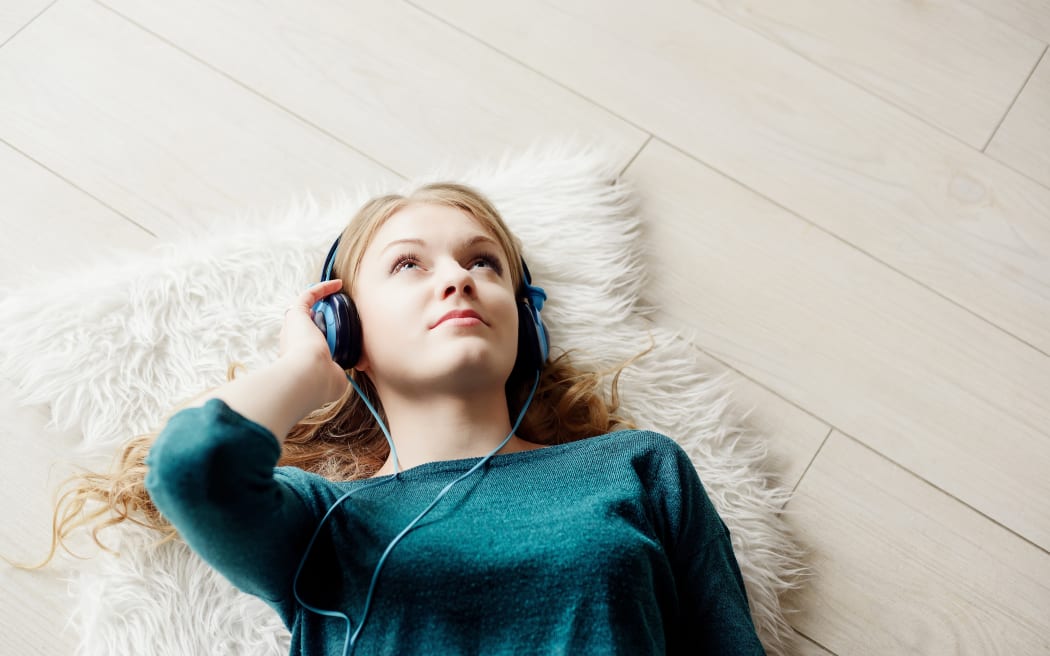 Beautiful blond woman listening to music through headphones. Lying on a wooden floor.