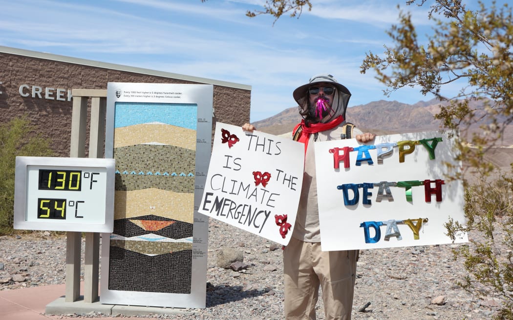 A protestor stands next to a digital display of an unofficial heat reading at Furnace Creek Visitor Center during a heat wave in Death Valley National Park in Death Valley, California, on July 16, 2023.