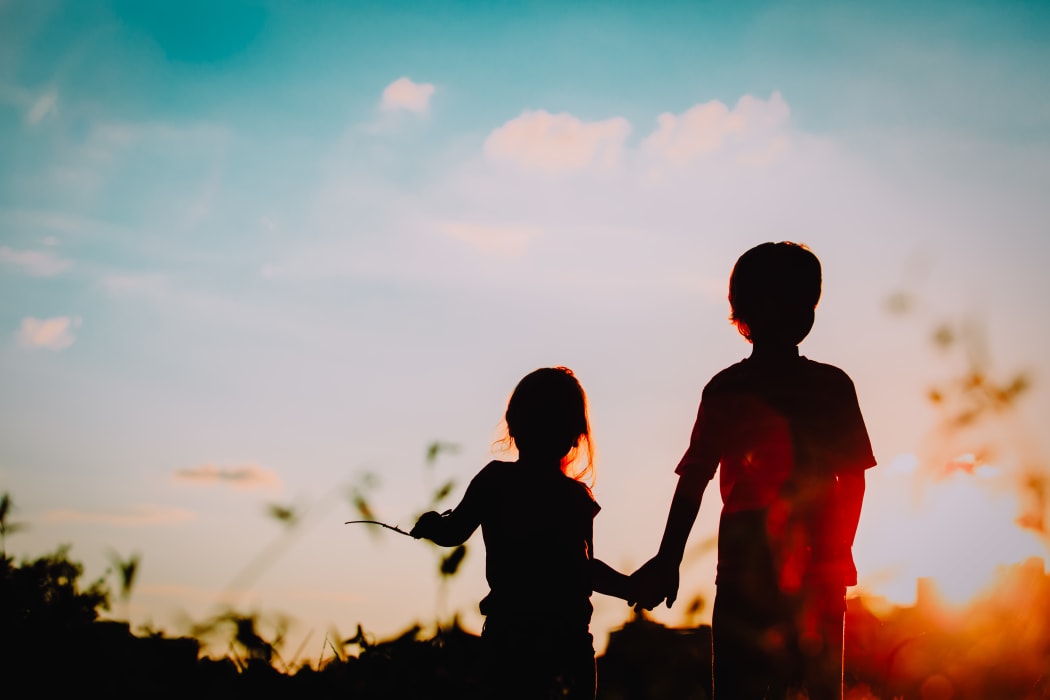 little boy and girl silhouettes holding hands at sunset nature