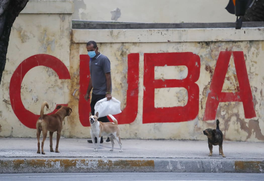 A man and dogs walk in front of a graffiti with the word "Cuba" in Havana, Cuba, on January 11, 2021.