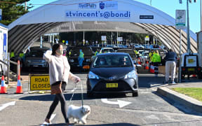 A woman walks her dog past the St. Vincent's Hospital drive-through testing clinic as health workers conduct COVID-19 tests at Bondi Beach in Sydney June 27, 2021, on the first full day of a two-week coronavirus lockdown